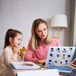 Mother and daughter applying cartoon astronaut waterproof stickers on a laptop