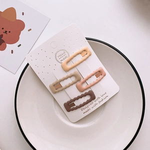 Set of four matte wave-shaped hair clips in pastel colors on a white plate display