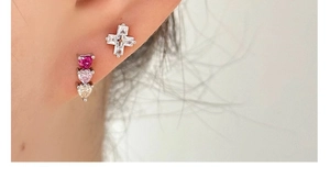 Macro shot of gradient heart earrings and a zircon cross stud on a model ear
