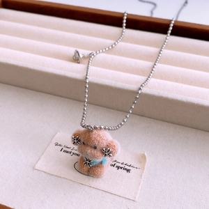 Macro view of plush puppy pendant with blue bow and silver chain on velvet tray