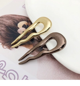 Detail of two minimalist U-shaped metal hairpins in gold and bronze on a ceramic plate