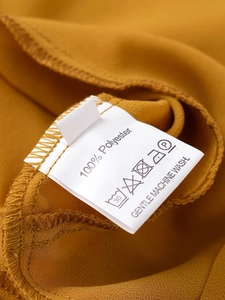 Detailed view of white wash care label on mustard fabric with 100% polyester information