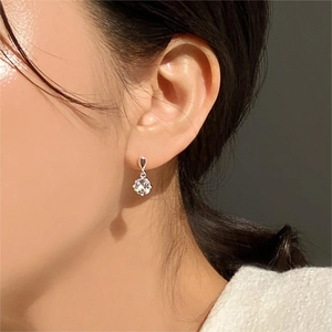 Close-up of a silver four-prong zircon earring worn on a ear with elegant drop design