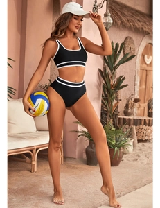 Detail of a two-piece bikini with black contrast piping and high-waisted shorts on a beach