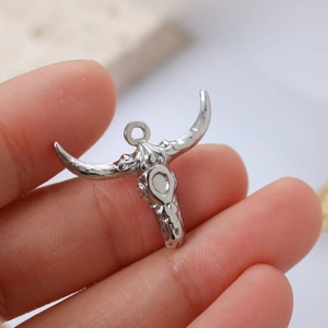 Close-up of silver stainless steel buffalo skull pendant held by fingers for scale
