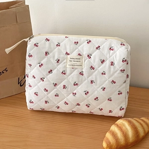 Detailed view of quilted white makeup bag with cherry pattern on a wooden background