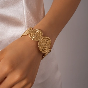 Vue détaillée d'un large bracelet doré à texture spirale porté au poignet
