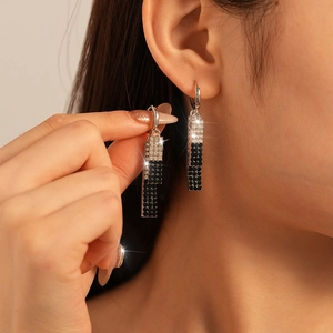 Détail de longues boucles d'oreilles argentées rectangulaires avec strass noirs et blancs
