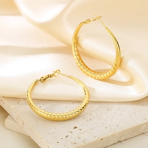 Macro detail of gold-plated stainless steel hoop earrings with textured spiral grooves