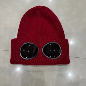 Detail shot of red knit beanie with integrated black goggles on a tiled background
