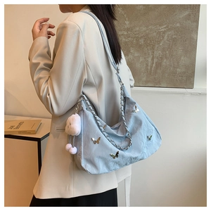 Detailed side view of light blue hobo bag with metal butterfly and plush ball pendant
