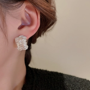 Close-up of silver metal hoop earring with unique irregular fold texture on female model