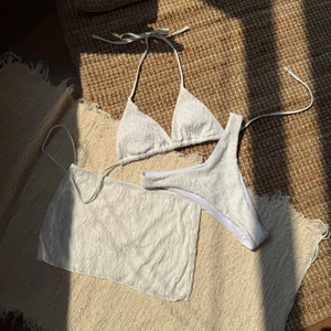 Flat lay of white three-piece bikini set with floral lace skirt on natural straw mat