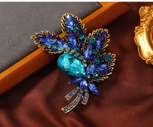 Detailed macro view of vintage gold leaf brooch with blue rhinestones and waterdrop gem