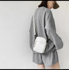 Model view of white minimalist nylon crossbody bag featuring textured leather and metal hardware