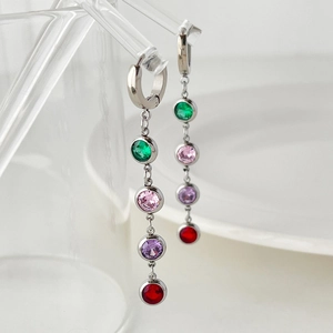 Macro shot of silver tassel earrings with colorful zircons on glass edge over white background
