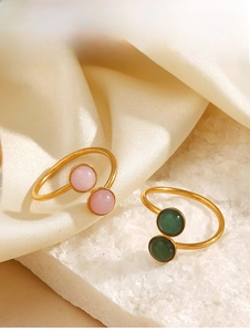Detail of adjustable gold rings with pink and green round gemstones on a white stone base