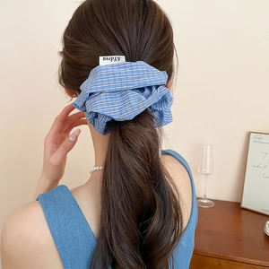 Blue and white checkered fabric scrunchie with woven tag on a ponytail hairstyle
