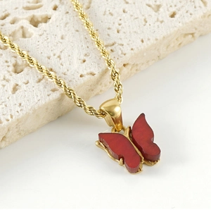 Detail of red butterfly pendant with gold twisted rope chain on textured stone