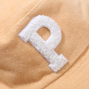 Détail macro du tissu éponge abricot avec un écusson brodé blanc en relief de la lettre P