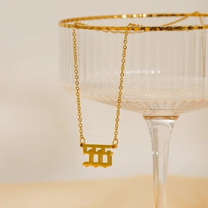 18K gold plated stainless steel number 555 pendant necklace hanging on a glass