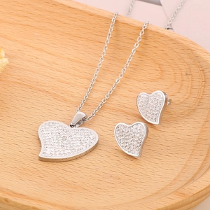 Close-up of heart-shaped necklace and stud earrings set with pavé rhinestones on wood