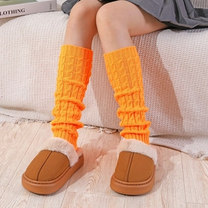Detailed knit texture of bright orange cable leg warmers paired with platform slippers