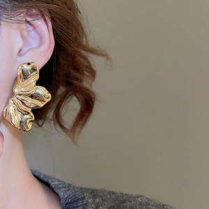 Close-up of golden irregular wavy earring on model showing unique abstract design