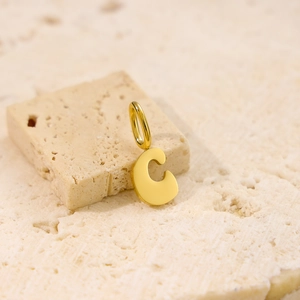 Macro shot of gold-plated letter C pendant on a beige stone with natural textures