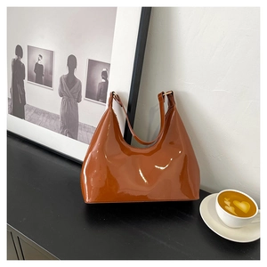 Polished brown patent leather hobo bag placed on a sleek black surface with coffee