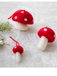 Macro view of three red wool felt mushroom ornaments in various sizes with pine branch