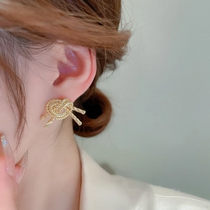 Detailed close-up of a golden rope knot earring worn by a model on the earlobe
