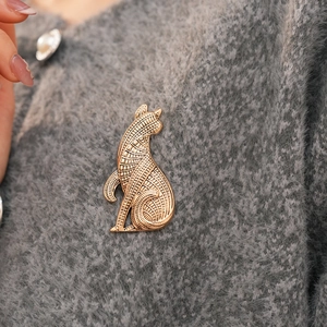 Nahaufnahme der goldenen Vintage Katzenbrosche mit gewebtem Muster auf grauem Stoff