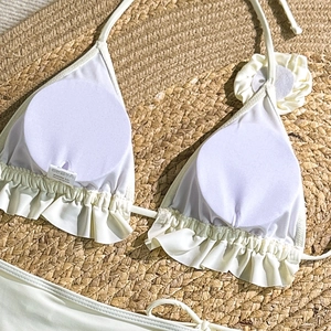 Detail of off-white bikini top with ruffle hem and 3D floral accent on beach straw mat