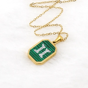 Gold malachite necklace with H-shaped crystal pendant on a white velvet surface