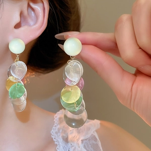 Close-up of dangling colorful resin disc earrings worn by a model in soft light