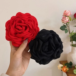 Detail showing red and black fabric flower hair claws held by hand for scale