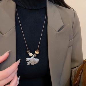 Detail of silver ginkgo leaf pendant with wooden beads on a brown braided necklace cord