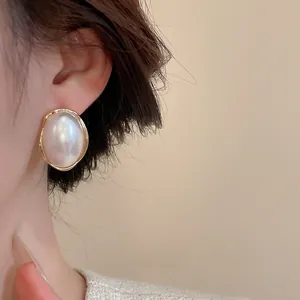 Close-up of elegant baroque pearl earrings with textured gold border on female model