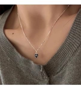 Detail view of s925 silver heart necklace with black enamel and bow on a model