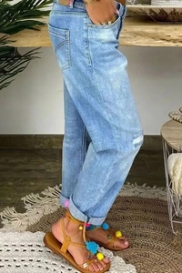 Vue latérale du jean droit bleu clair déchiré avec des sandales à pompons colorés