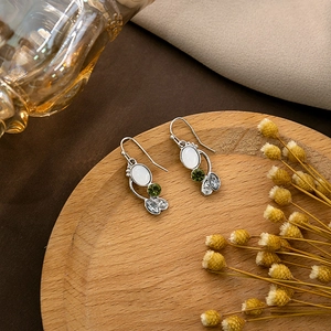 Detailed close-up of retro silver drop earrings with emerald and opal gemstones on wood
