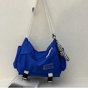 Blue nylon messenger bag detail with white strap and checkerboard plush charm accessory