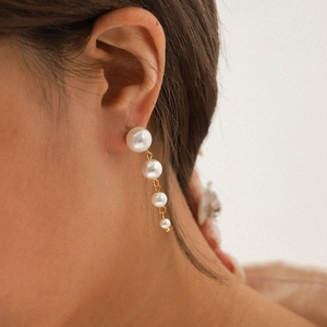 Elegant gold stainless steel drop earrings featuring four graduated pearls on a model