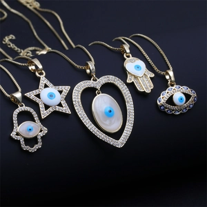 Detail of five gold necklaces featuring Hamsa hand, heart, and evil eye charms with blue accents