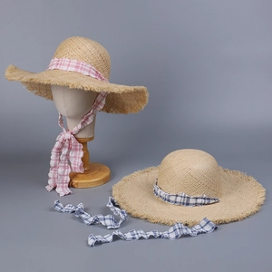 Detail of raffia sun hat featuring blue and pink checkered ribbons and frayed edge brim