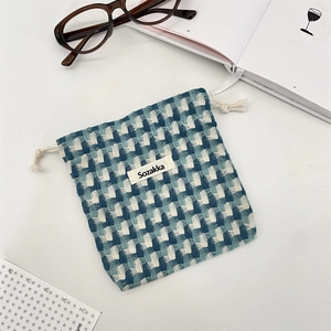 Détail d'une pochette tissée à carreaux bleu et vert avec cordons en coton sur bureau