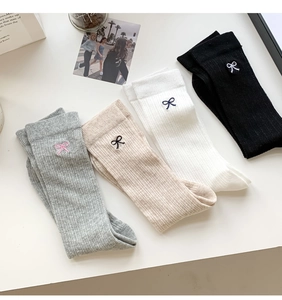 Detailed view of four pairs of ribbed socks in grey, beige, white, and black with bows
