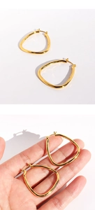 Close-up of geometric 24k gold plated brass earrings shown on a model hand for scale