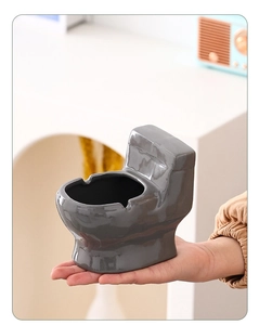 Close-up of a grey toilet-shaped ceramic ashtray held in hand with glossy finish detail